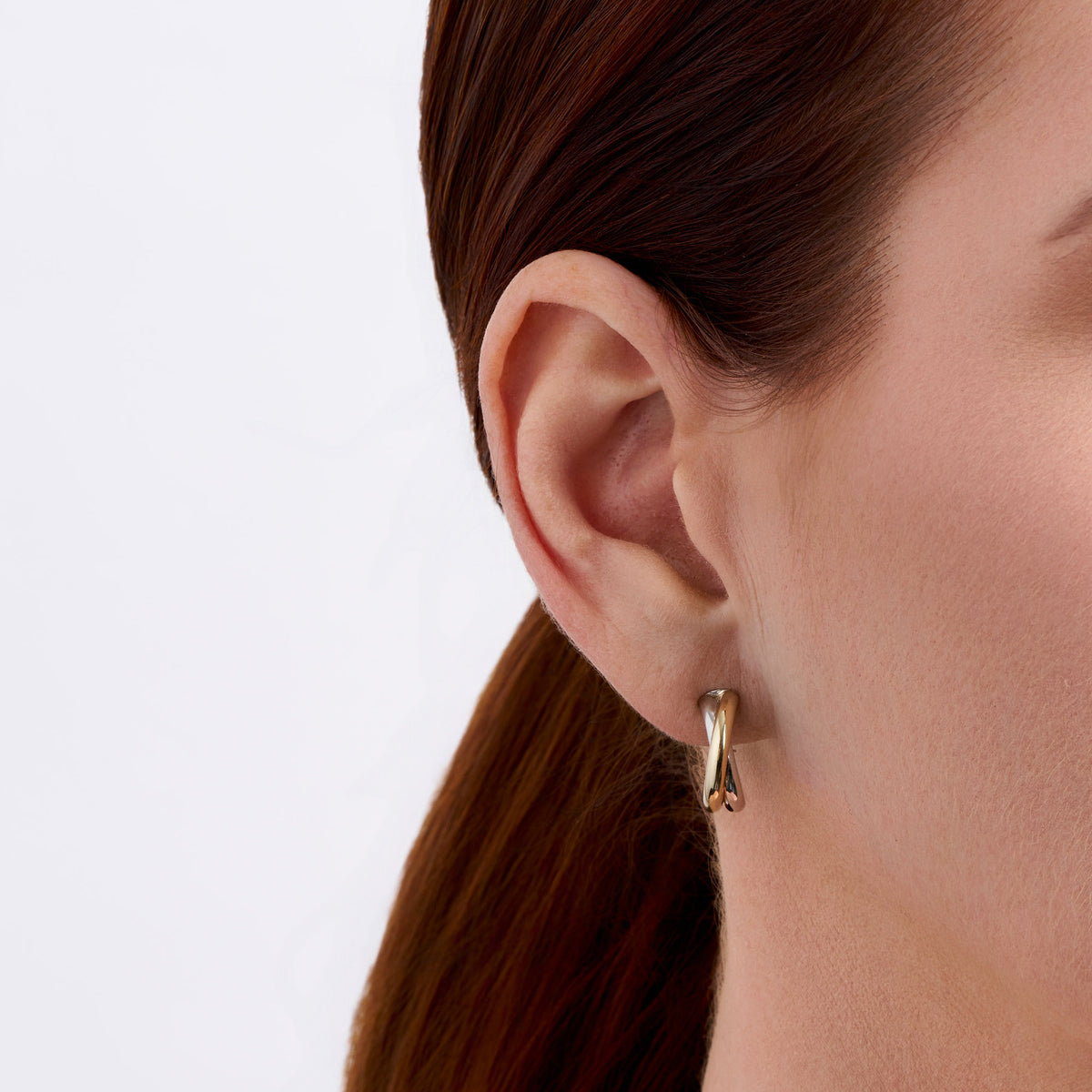 On-body view of a model wearing the Wallace Bishop Crossover Hoop Earrings in Sterling Silver & 9ct Yellow Gold, with the petite two-tone crossover hoops at the earlobe.