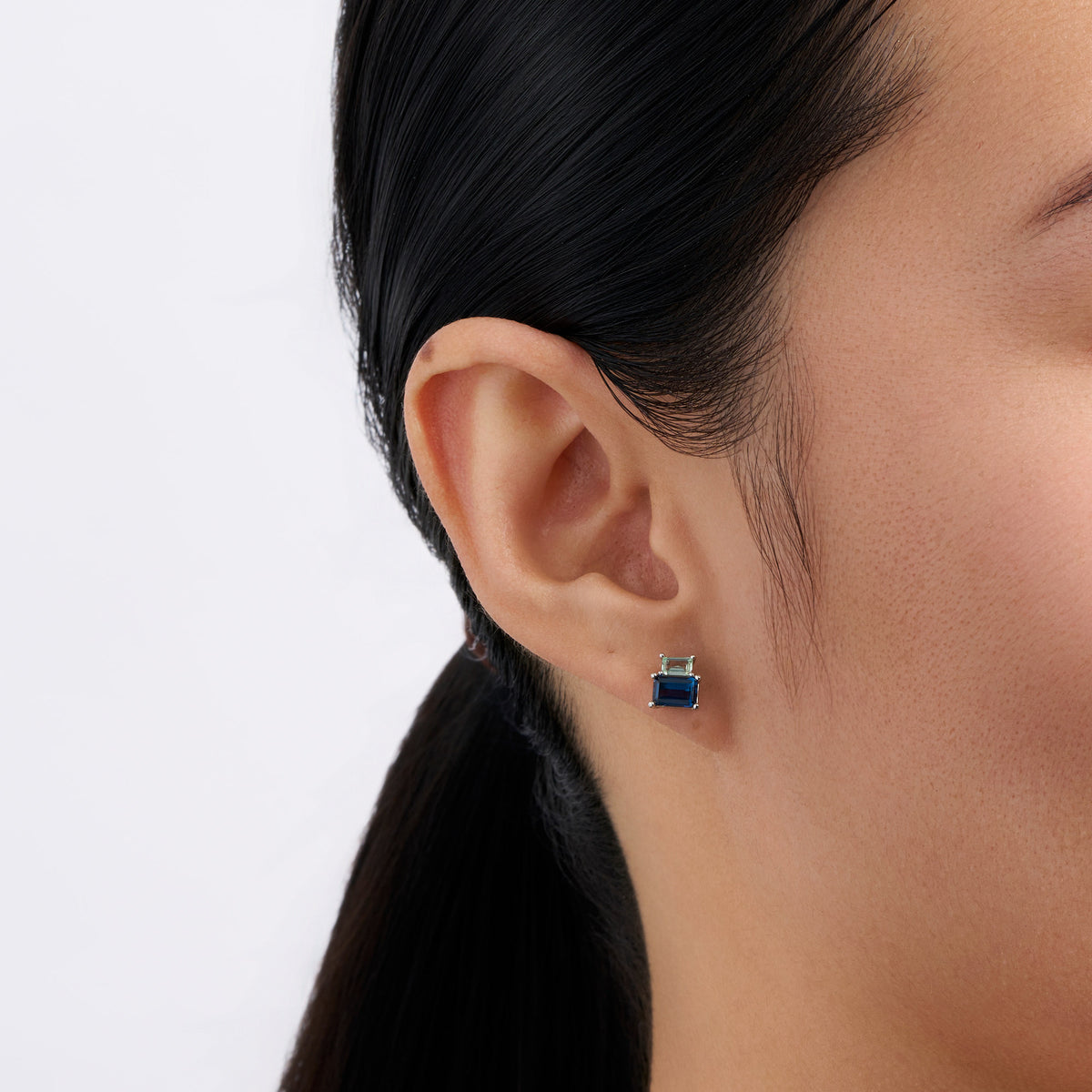 On-body view of a model wearing the Wallace Bishop Cubic Zirconia Stud Earrings in Sterling Silver, with the light blue and mint emerald cut cubic zirconias in each earlobe.