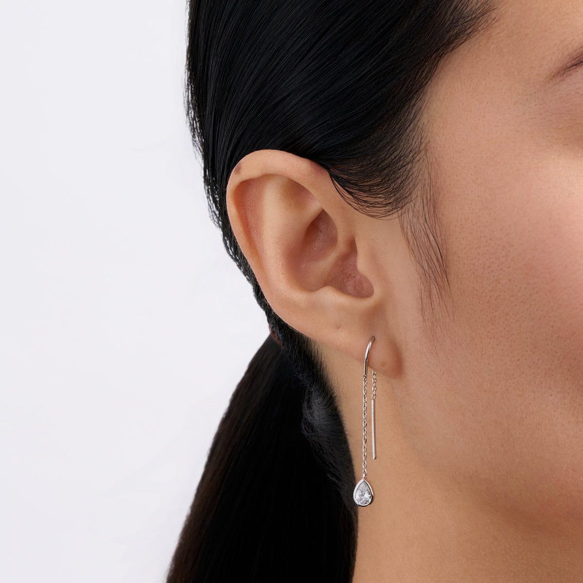 On-body view of a model wearing the Wallace Bishop Cubic Zirconia Bezel Threader Earrings in Sterling Silver, with the fine chain threaded through the piercing and the pear cut cubic zirconia drop hanging below the earlobe.