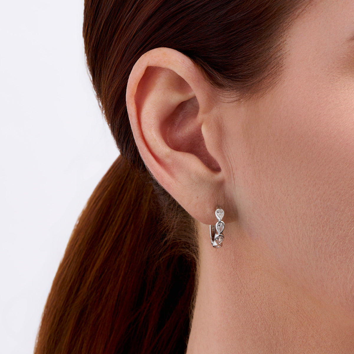 On-body view of a model wearing the Wallace Bishop Cubic Zirconia Bezel Huggies in Sterling Silver, hugging the earlobe with bezel-set pear cut white cubic zirconias.