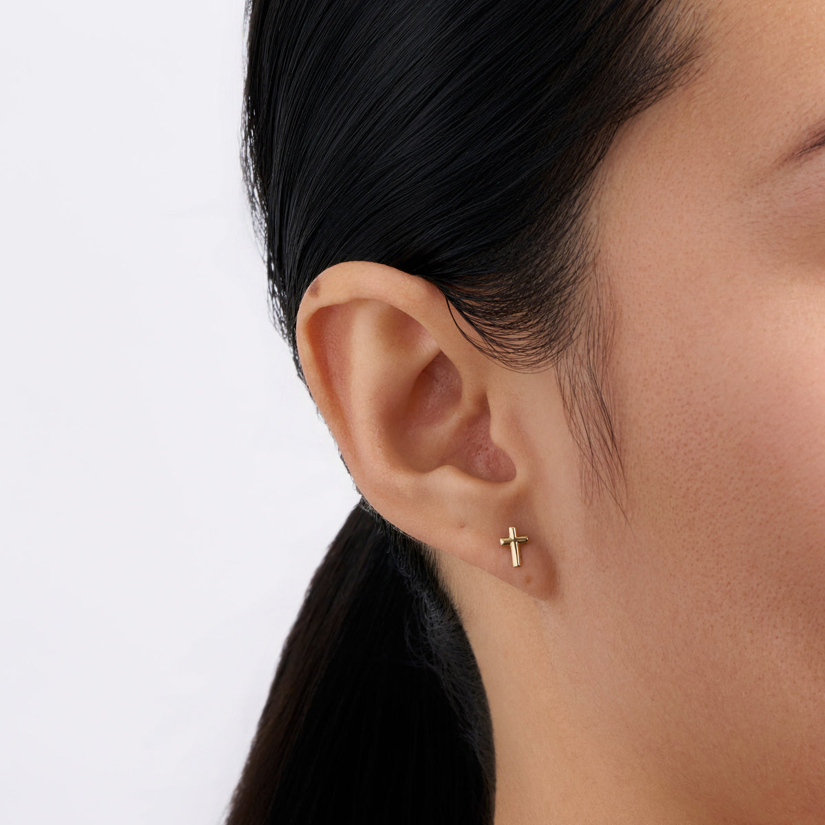 On-body view of a model wearing the Wallace Bishop Cross Stud Earrings in 9ct Yellow Gold, 6.75mm in length, with a polished gold cross in each earlobe.