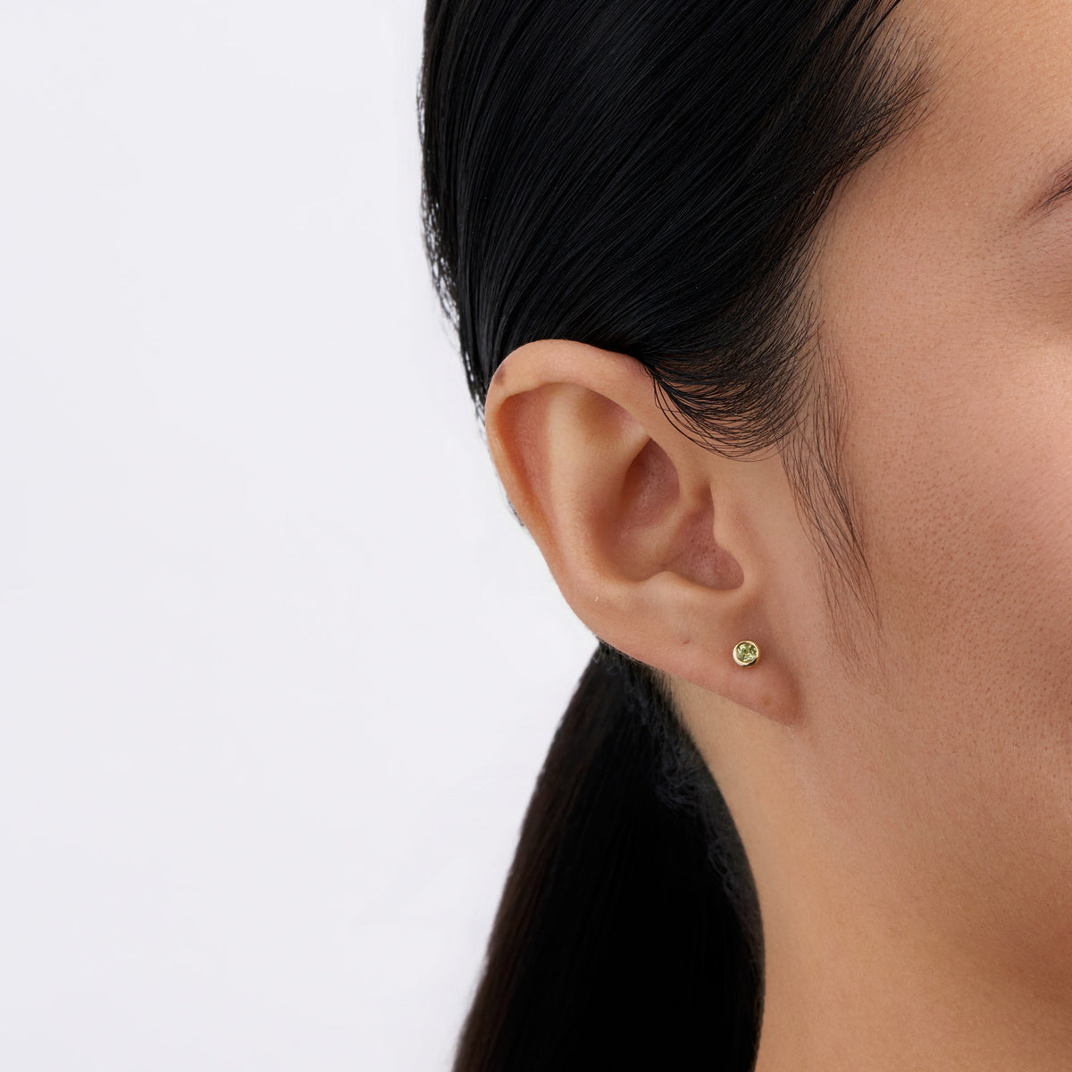 On-body view of a model wearing the Wallace Bishop Peridot Bezel Stud Earrings in 9ct Yellow Gold, with a 3mm round peridot in each earlobe.