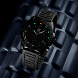 Luminox Pacific Diver Chronograph Men's 44mm Quartz Watch XS.3141.BO.1 shown in a coastal outdoor setting. This Pacific Diver Chronograph features an all-black design, a CARBONOX™ dive bezel and 200m water resistance.
