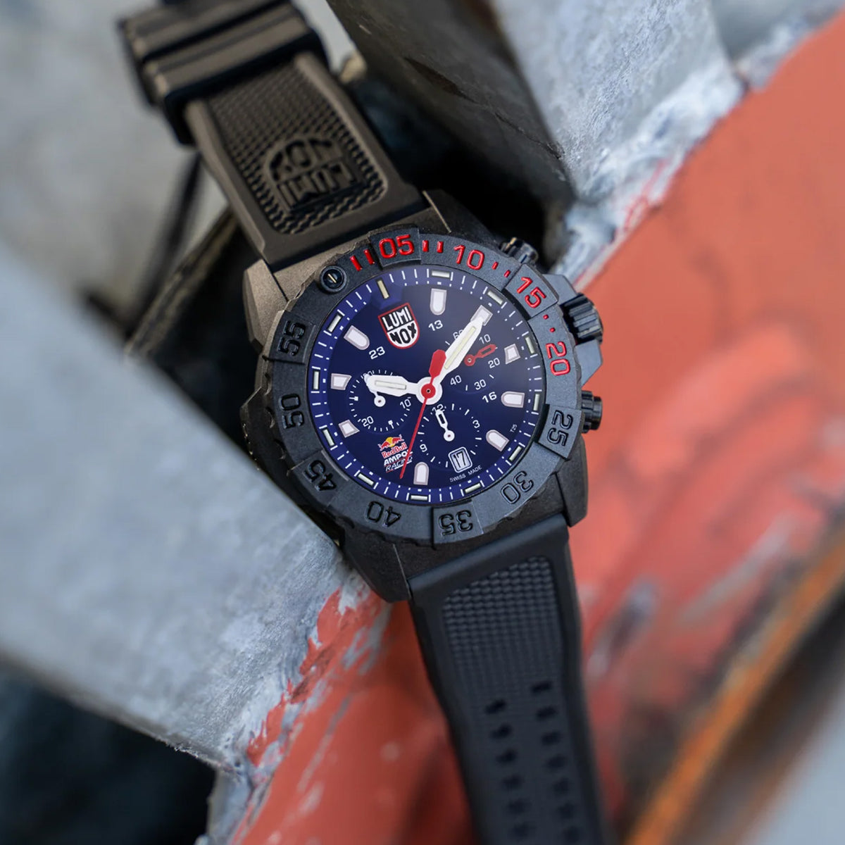 Luminox Navy SEAL Red Bull Ampol Racing Edition Men's 43mm Quartz Chronograph Watch XS.3581.EY.ARB shown in a motorsport-inspired setting. This limited edition chronograph features Red Bull Ampol Racing branding, a lightweight CARBONOX™ case and 200m water resistance.