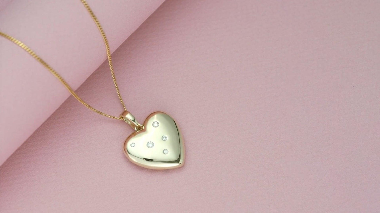 flatlay image of a golden heart pendant necklace with bezeled diamond gemstones