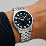 The Loyal Adventurer Pilot Watch worn on the wrist, showing the true scale of the 40mm case and black dial. The stainless steel finish and 12 o'clock orientation triangle give this quartz watch a distinctive, versatile look for daily wear, alongside the bonus black leather strap included with this set.