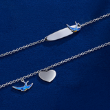 The Wallace Bishop Bluebird of Happiness Heart Bracelet in Sterling Silver for children, reference 32BLBB01, measuring 160mm in length, shown together with the Bluebird of Happiness ID Plate Bracelet in Sterling Silver, reference 32BTBB01, on a 160mm cable chain. The heart bracelet features a blue enamel bluebird and a polished silver heart as solid charms, and the ID plate bracelet features a 5mm engravable plate with a bluebird detail in blue enamel.