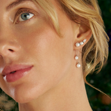 On-ear view of a model wearing the Wallace Bishop Pearl & Cubic Zirconia Drop Earrings in Sterling Silver, reference 33ESCZ32. A pear cut cubic zirconia and two graduated white pearls sit along the ear, with two fine chains hanging below the earlobe, each ending in a white pearl.