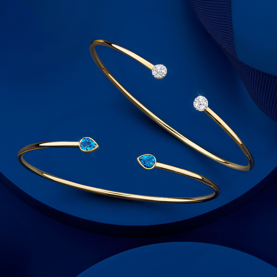 Front-on view of two Wallace Bishop flexi bangles in 9ct Yellow Gold on a plain background: the 0.15 TW Diamond Pavé Flexi Bangle, reference 3BG015Y, with pavé set diamonds, and the London Blue Topaz Flexi Bangle, reference 93BGLTBY, a cuff-style bangle measuring 50mm by 60mm with a bezel-set 5x4mm natural pear-cut London blue topaz on each side.