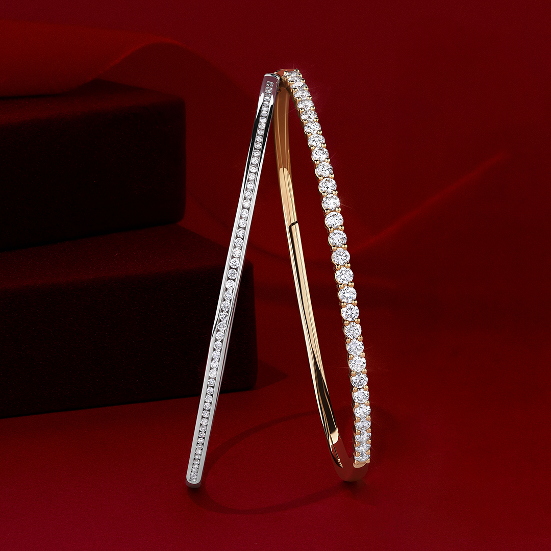 Front-on view of two Wallace Bishop round diamond bangles: the 1.00 TW Diamond Bangle in 9ct White Gold, reference 3BG100DW, and the 2.00 TDW Diamond Oval Bangle in 9ct Yellow Gold, reference 3BBGCL200Y. Both bangles are set with round cut diamonds.