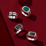 Flat lay view of four gents rings in sterling silver: the Hardy Brothers Princess-Cut Black Spinel Gents Ring, reference 4URG5BSSSV, 6.5mm in width, with a channel-set stripe of princess-cut black spinel through the middle, the Hardy Brothers Malachite Gents Signet Ring, reference 4URRP002V, with a cushion-shaped green malachite and rope detailing on the shoulders, the Wallace Bishop Elongated Onyx Gents Signet Ring, reference 4URG1BASSV, with a 15mm by 10mm octagonal black onyx and rope detailing on the sh