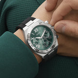 Close-up of a person wearing a Guess watch with a green face and black strap.