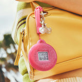 The Casio Baby-G BGD10KG-4D centre case removed from the bezel and inserted into the included customisable silicone holder with acrylic panels — shown as a bag charm or waist accessory with the rotating pixel-art animations visible on the LCD display.