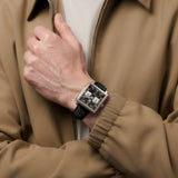 TAG Heuer Monaco Chronograph CDW2150.FC8360 shown worn on the wrist, illustrating the square case's proportions and leather strap fit. The black dial and rose gold accents stand out against the tan jacket sleeve in frame.