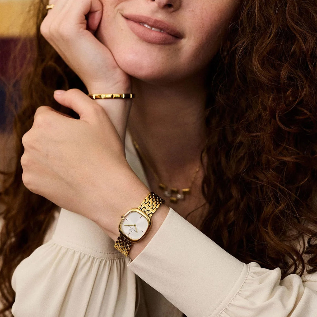 Lifestyle image of the Daniel Wellington Corta Grain-Link Women’s 24mm Quartz Watch DW00100993 styled with gold jewellery. The warm gold tone layers easily with gold bracelets and rings.