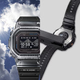 Casio G-LIDE GBXH5600-1D Black Digital Watch photographed at an angle in an outdoor setting with a dynamic background. Square case profile and black resin band detail shown against a sky and water backdrop.