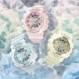 Three G-Shock watches in pink, white, and yellow on a textured blue and white background.