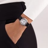 Hamilton American Classic Cushion Mechanical Women’s 30mm Watch H36109710 is worn on the wrist with its black leather strap fastened. The compact square case and white dial suit a classic dress watch look.