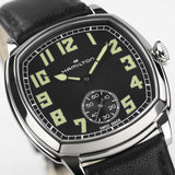 Hamilton American Classic Cushion Mechanical Unisex 34mm Watch H36129730 is shown in close up, revealing the square-style numerals, railway minute track and small seconds sub-dial. The slim hands stand out against the black dial.