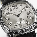 Hamilton American Classic Cushion Mechanical Unisex 34mm Watch H36149710 is shown in close up, revealing the square-style numerals, railway minute track and small seconds sub-dial. The slim hands stand out against the white dial.