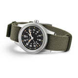 Hamilton Khaki Field Mechanical 36mm Watch H69399930 is shown at a 3/4 angle, highlighting the acrylic box glass, black dial, and khaki NATO strap together. The angle showcases the watch's rugged, purpose-built military design produced exclusively throughout 2026.