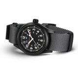 Hamilton Khaki Field Mechanical 38mm Watch H69409930 is shown at a 3/4 angle, highlighting the sapphire crystal, black dial, and NATO strap together. The angle showcases the watch's faithful recreation of its 1960s military field watch origins.