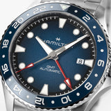 Hamilton Khaki Navy Scuba Auto GMT 43mm Watch H82535140 is shown at a 3/4 angle, highlighting the sapphire crystal, blue dial, and ceramic GMT bezel together. The angle showcases the watch's travel-ready, diving-inspired design.