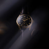 The Seiko Presage wristwatch with a black dial, gold-tone numerals and hands, and a bronze-toned case, shown against a dark moody background with dramatic light beams.