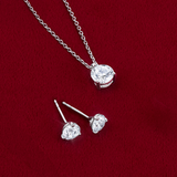 Flat lay view of the Wallace Bishop 1.00 TDW Round Lab-Grown Diamond Solitaire Pendant in Sterling Silver, reference LGPDSS100, on a 500mm (approximately 19.7 inch) fine cable chain, laid flat with the 1.00 TDW Round Lab-Grown Diamond Solitaire Stud Earrings in Sterling Silver, reference LGERSS100. Each piece features a round lab-grown diamond in a three-claw setting, and the earrings are secured with butterfly backs.
