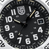 Close-up of a Luminox watch dial with a black face, large white Arabic numerals, black hands with silver tips, a date window at 3 o'clock, and a white bezel.