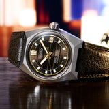 The King Seiko Vanac Automatic Men's 41mm Watch SLA093J features a dark brown dial with golden accents, LumiBrite hands and indexes, and a date window. The 41mm stainless steel case is fitted with box-shaped sapphire crystal.