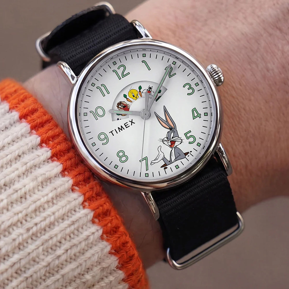 The Timex x Looney Tunes Weekender Quartz 40mm Watch TW2Y99100 pairs its silver-tone case with a black fabric strap on the wrist. The 40mm size gives it a relaxed, casual look.
