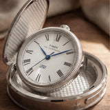 The Timex Waterbury America 250 Table Clock TW6A05900 makes a distinguished tabletop display piece, shown here open on a wooden surface. The commemorative design suits collectors and fans of American history alike.