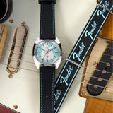 The Timex x Fender Quartz 37mm Watch TWG068900 is shown displayed across a Fender electric guitar. The silver-tone case and black strap suit guitar players and Fender fans alike.