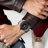 TAG Heuer Formula 1 Date WAZ1110.BA0875 shown worn on the wrist, illustrating the case proportions and steel bracelet fit. The black dial stands out against the sleeve in frame.