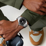 TAG Heuer Formula 1 Date WAZ1112.BA0875 shown worn on the wrist, illustrating the case proportions and steel bracelet fit. The black dial stands out against the olive jacket sleeve in frame.