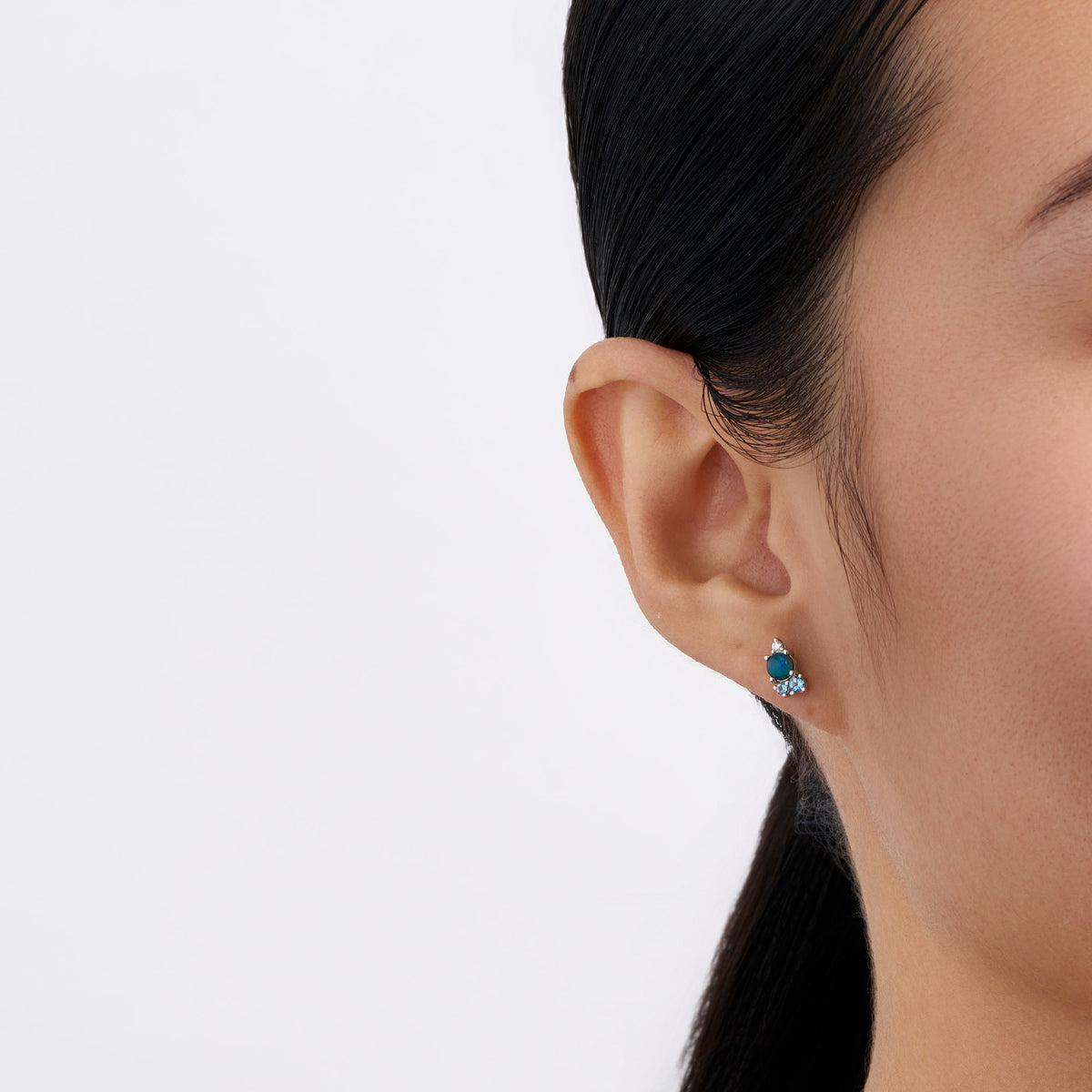 On-body view of a model wearing the Wallace Bishop Triplet Opal, Swiss Blue Topaz, London Blue Topaz & Lab-Grown-Diamond Cluster Stud Earrings in Sterling Silver, with a gemstone cluster in each earlobe.