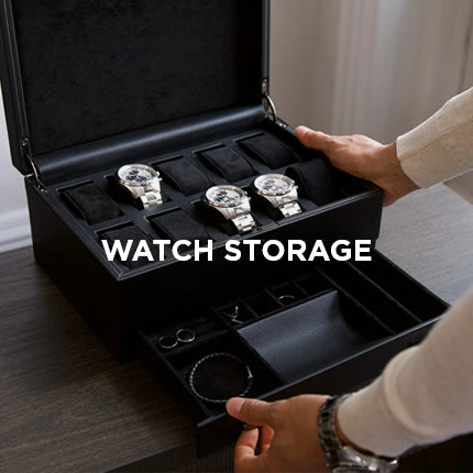 Black watch storage box with three silver watches inside, held by a person.