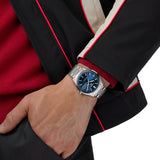 TAG Heuer Carrera Day-Date WDA2112.BA0043 shown worn on the wrist, illustrating the case proportions and steel bracelet fit. The blue dial stands out against the dark jacket sleeve in frame.
